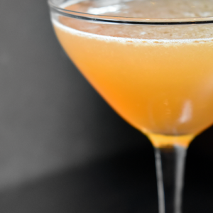 A close up of an orange drink in a wine glass.